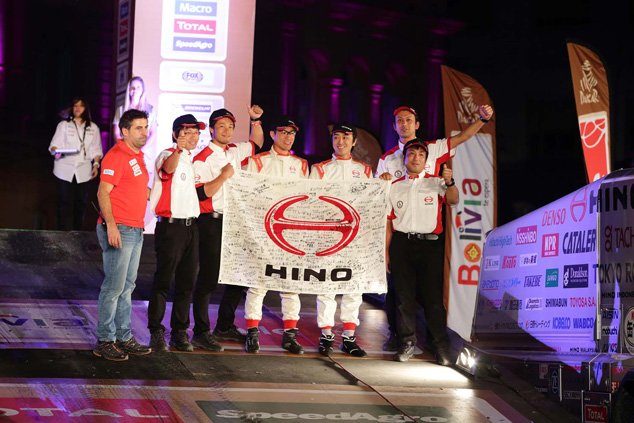 The Car 2 crew and mechanics pose for a photo by the podium on stage.